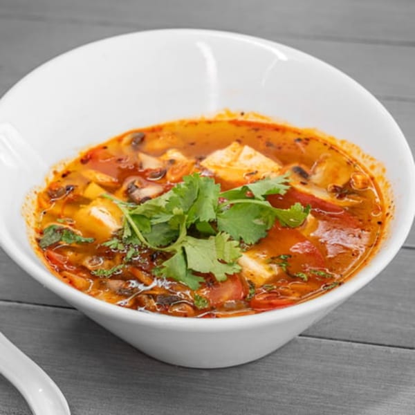 A white bowl filled with vibrant vegan Tom Yum soup, garnished with fresh cilantro.