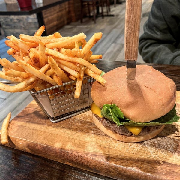 A vegan burger with cheese and lettuce, skewered with a knife, next to a basket of fries.