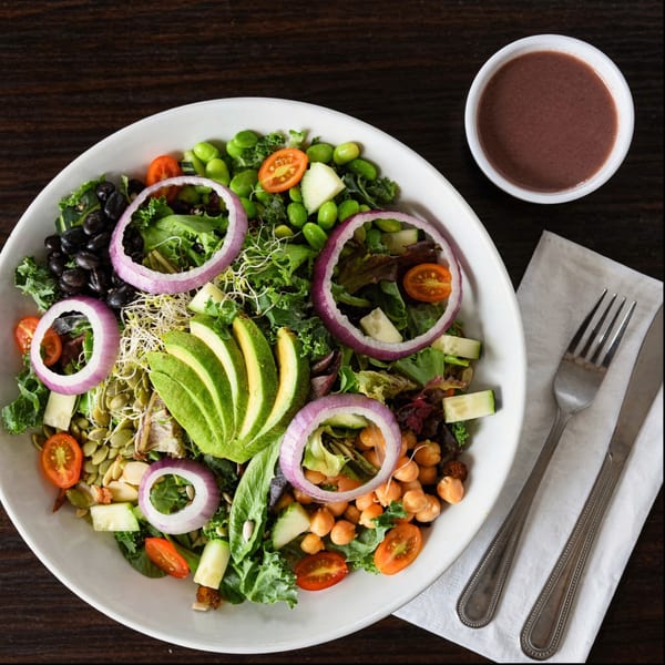 A vibrant vegan salad with avocado, black beans, chickpeas, and red onion, with dressing on the side.