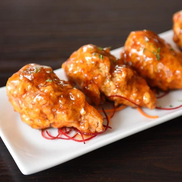 Vegan buffalo wings, glazed with orange sauce and garnished with herbs, on a white rectangular plate.