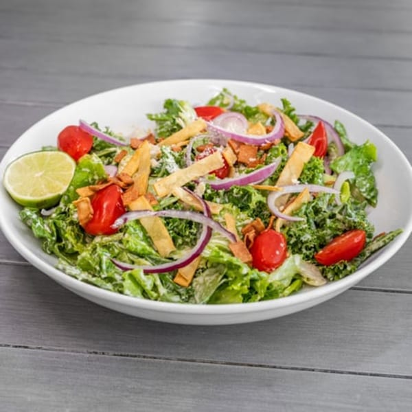 Vegan salad with lettuce, red onions, cherry tomatoes, tortilla strips, and a lime wedge.