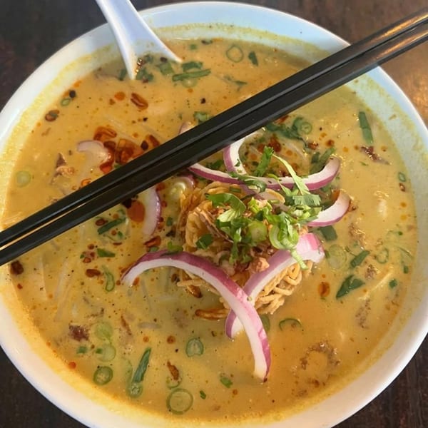 Vegan curry noodle soup with red onions, cilantro, and crispy noodles, with chopsticks resting on top.