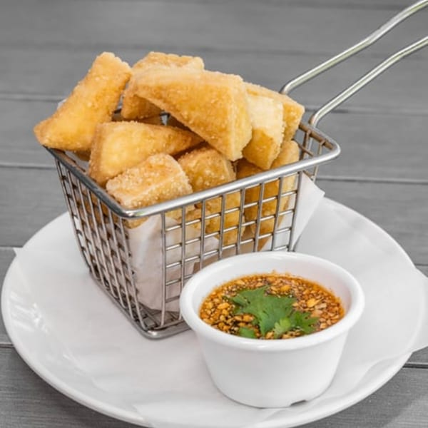 Crispy golden vegan tofu bites in a metal basket with a side of dipping sauce.